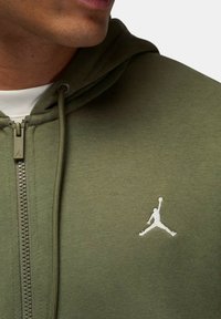 Felpa con cappuccio verde oliva con zip, realizzata in tessuto morbido, con logo Jumpman bianco sul petto a sinistra e coulisse sul cappuccio.