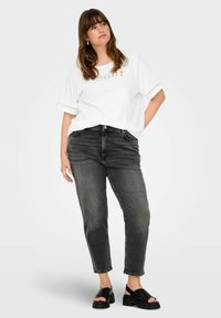 Witte t-shirt met decoratieve letters en kantaccenten, gecombineerd met hoog-gewone, donkergrijze jeans en zwarte platform sandalen.
