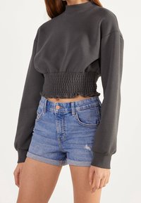 Sudadera gris recortada con cintura fruncida y mangas largas, combinada con pantalones cortos de denim desgastado de talle alto con dobladillos enrollados.