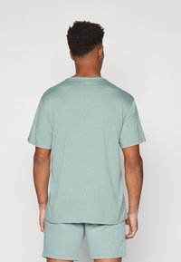 Tricou scurt mint green, cu guler rotund, dintr-un material moale, expus din spate, asortat cu pantaloni scurți de aceeași culoare.