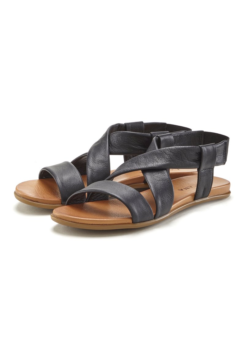 Schwarze Leder-Sandalen mit breiten Kreuzgurten und Rückenstütze, mit einer flachen, tanfarbenen Sohle und glatter Oberfläche. Geeignet für lässige Trageanlässe.