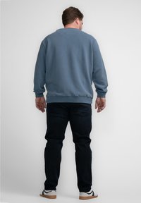 Blauwe sweatshirt met een ronde halslijn, geribbelde manchetten en zoom. Gecombineerd met donkere jeans en witte sneakers. Uitzicht is vanaf de achterkant.
