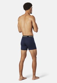 Navy blue boxer shorts made of soft fabric with a black waistband featuring "Smartwool" logo. Model viewed from the back, barefoot.