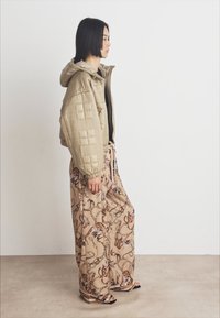 Padded beige jacket with geometric quilted texture, paired with wide-leg beige pants featuring a brown chain pattern.