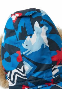 Geïsoleerde muts met een blauwe, gemusterde stof die abstracte vormen in rood en wit bevat. Afgewerkt met nepbont aan de randen.