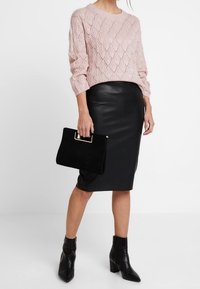 Maglione lavorato a maglia rosa chiaro con un motivo a rombi, abbinato a una gonna in pelle nera a tubino. Tiene una borsa a tracolla in suede nero. Stivali neri alla caviglia.