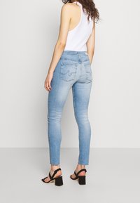 Jeans ajustados de color azul claro con una cintura de tiro medio, que cuentan con bolsillos traseros y un leve desvanecimiento. Combinados con sandalias negras de tacón cuadrado.