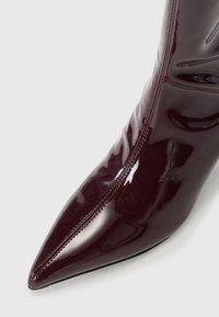 Bordeaux patenten leren enkellaarsjes met een puntige neus en een ritssluiting aan de zijkant. Heeft een gladde, glanzende afwerking en een minimalistisch ontwerp.