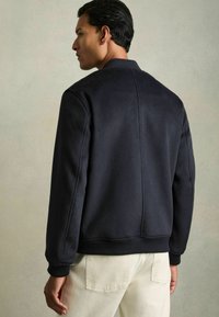 Marineblauwe sweatshirt met een geribde kraag en manchetten, met een strak ontwerp. Gemaakt van zachte stof met een gestructureerde afwerking. Achteraanzicht weergegeven.