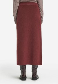 Burgundy stickad midiklänning med ett texturerat mönster, hög midja och åtsittande silhuett, i kombination med glansiga svarta knähöga stövlar.