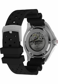 Timex watch with a silver stainless steel case and a black rubber strap. Transparent case back reveals intricate movement details.