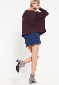 Bordowy, oversize sweter o luźnym kroju, zestawiony z jasnoniebieską spódnicą dżinsową i szarymi botkami za kostkę z zamkiem błyskawicznym.