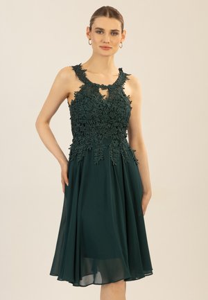 Grünes Kleid mit floralen Spitzendetails am Oberteil, ärmellosem Design und einem A-Linien-Rock aus fließendem Stoff.