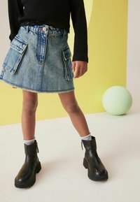 Jeanskjol med två framsidiga cargo-fickor, fransad nederkant och en ljusblå tvätt. Svarta ankelboots med tjock sula och silverdetaljer i dragkedjan.