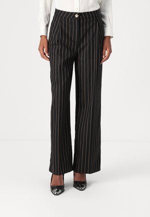 Pantaloni neri a gamba larga con strisce verticali arancioni, dotati di una vita alta e di un accento decorativo in argento nella parte anteriore.