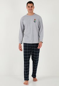 Cămașă gri cu mâneci lungi, cu un grafic colorat de desene animate pe piept, asortată cu pantaloni de pijama în carouri bleumarin. Material din amestec de bumbac.