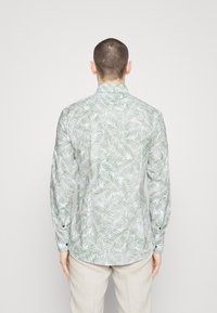 Langsleeve shirt met een groenbladpatroon op een witte achtergrond, gemaakt van lichte stof met een knoopsluiting aan de manchetten.