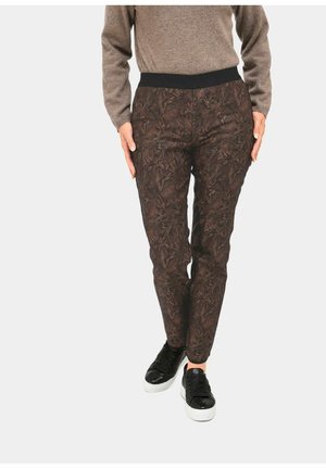 Pantaloni a righe marroni con vita elastica nera, caratterizzati da un motivo floreale e vestibilità affusolata. Indossati con sneakers nere.