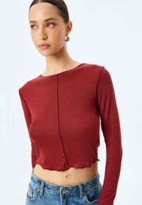 Burgunderröd ribbad långärmad topp i cropped-modell med rundad halsringning, som har en rå kant och en central sömdetailj. Matchas med denimshorts.
