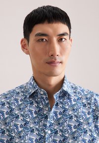 Overhemd met lange mouwen en knopen, met een witte basis en ingewikkelde blauwe paisley-patronen, puntkraag en een zachte katoenen textuur.