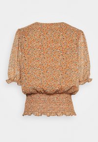 Blusa floreale beige con maniche a sbuffo, vita smock e orlo arricciato. Presenta motivi floreali arancioni, blu e neri su un tessuto leggero.