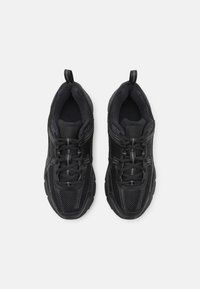 Chaussures de sport noires avec une tige en maille et synthétique, col rembourré, semelle texturée et accents réfléchissants. Lacets maintenus par des accessoires en plastique.