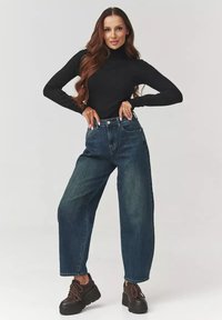 Czarny golf w połączeniu z jasnoniebieskimi dżinsami o wysokim stanie i luźnym kroju oraz masywnymi czarnymi butami na platformie.