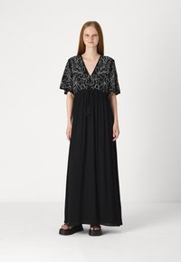 Rochie maxi neagră cu mâneci scurte, având un design brodat floral în alb, decolteu în formă de V și o talie ajustabilă cu șnur cu ciucuri.