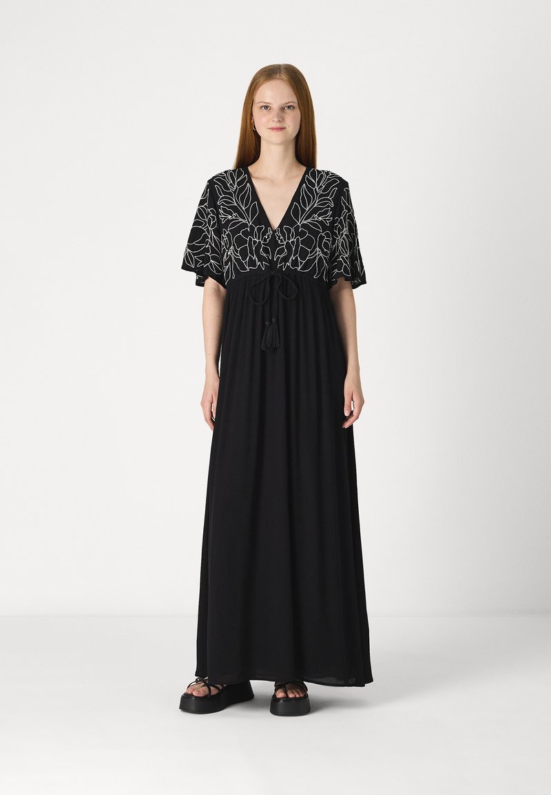 Rochie maxi neagră cu mâneci scurte, având un design brodat floral în alb, decolteu în formă de V și o talie ajustabilă cu șnur cu ciucuri.