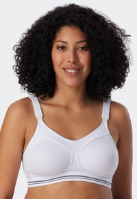 Bralette bianco con spalline regolabili, tessuto liscio e coppe sagomate. Presenta una fascia grigia a righe nella parte inferiore per un supporto extra.
