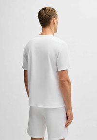 Wit T-shirt met korte mouwen gemaakt van gestructureerde stof, met een rechte snit, ronde hals en bijpassende korte broek zichtbaar op de achtergrond.