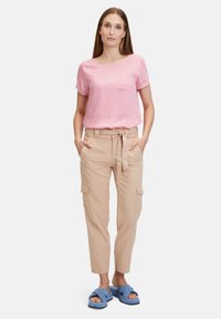 Helles rosa T-Shirt mit kurzen Ärmeln und einer Brusttasche, kombiniert mit beigen Cargo-Hosen mit gebundenem Bund und Seitentaschen, getragen mit blauen Schlappen.