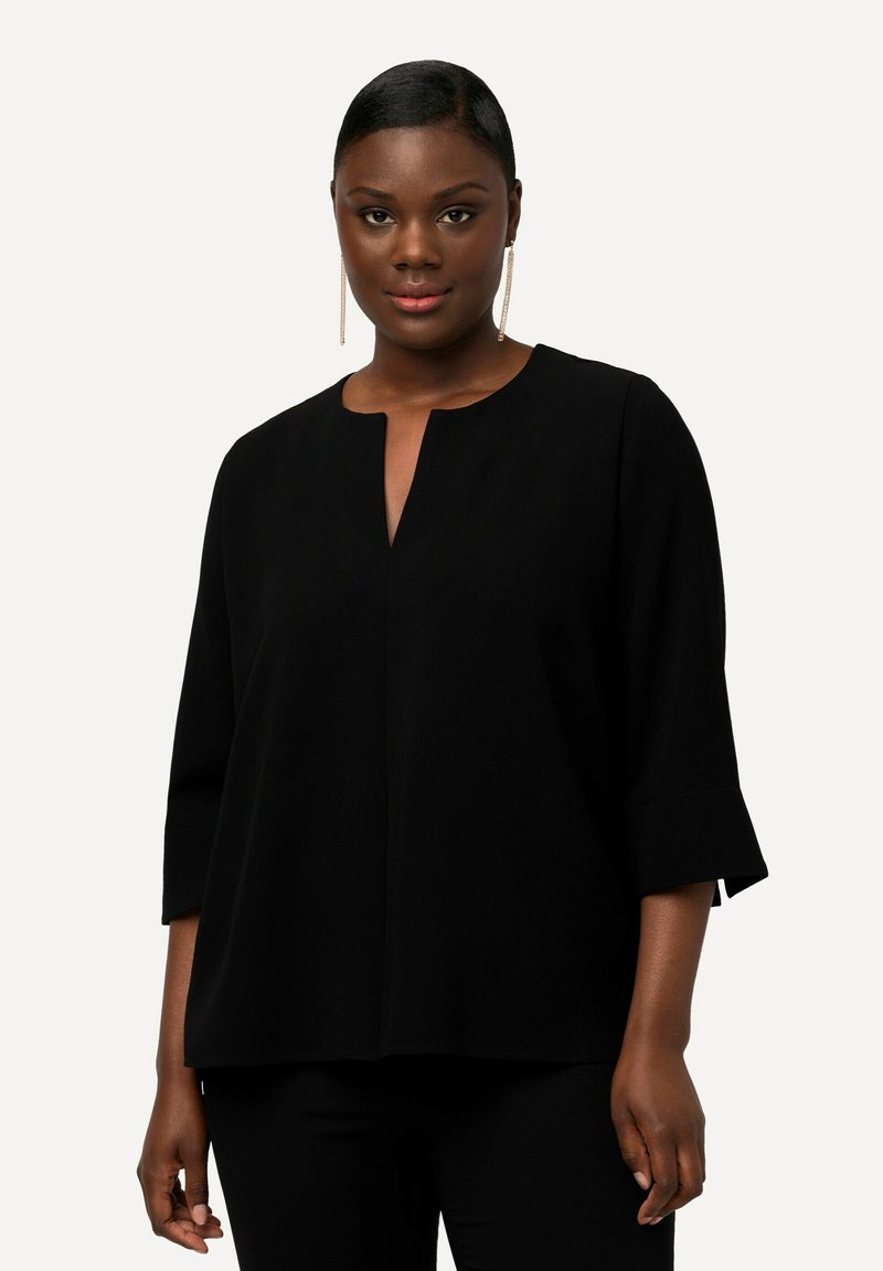 Top nero a vestibilità ampia con scollo rotondo, maniche a tre quarti e dettaglio con spacco frontale. Tessuto liscio e design minimalista.