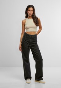 Beige gerippter Crop-Top kombiniert mit hochgeschnittenen schwarzen Jeans. Die Jeans haben einen geraden Schnitt und kontrastierende Nähte. Weiße Sneaker sind sichtbar.