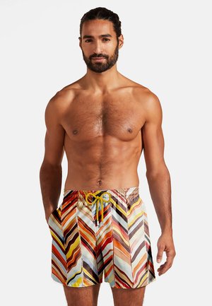 Swim shorts with a multicolored zigzag pattern, featuring a yellow drawstring and side pockets, made from lightweight fabric.