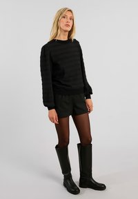 Maglione nero a trama con maniche lunghe, abbinato a pantaloni corti neri e collant trasparenti, completato da stivali neri al ginocchio.