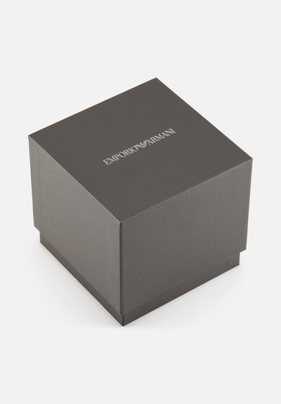Geschlossene dunkelgraue quadratische Emporio Armani-Box, schräg vor einem schlichten hellen Hintergrund.
