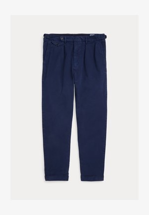 Niebieskie granatowe casualowe spodnie z plisowanym przodem, bocznymi kieszeniami, zapinanymi regulacjami w pasie i podwiniętymi mankietami, rozłożone na jasnym tle.