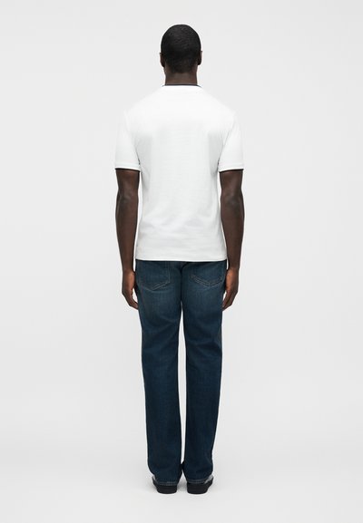 Λευκό T-shirt με κοντά μανίκια και στρογγυλή λαιμόκοψη, συνδυασμένο με σκούρο μπλε τζιν παντελόνι με ευθεία γραμμή και ορατές πίσω τσέπες.
