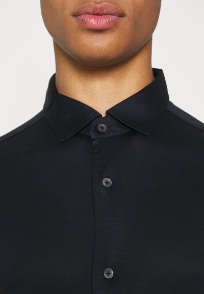 Camicia nera con colletto, realizzata in tessuto liscio, caratterizzata da una patta con tre bottoni neri e un design del colletto strutturato.