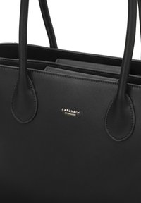 Sac fourre-tout en cuir noir avec deux longues poignées, présentant une texture lisse et un accent logo doré centré sur le devant.