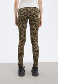 Luipaardprint legging in bruin en zwart, aansluitend ontwerp, zachte textuur, gecombineerd met zwarte sport schoenen, zicht van achter.