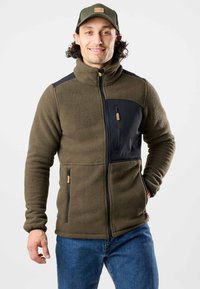 Fleecejacke in Olivgrün mit schwarzen Akzenten. Merkmale sind ein hoher Kragen, vordere Reißverschlusstaschen und ein strukturiertes Gewebe für Wärme und Komfort.