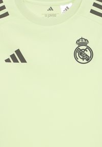Svetlozelené športové tričko vyrobené z hladkej tkaniny, s čiernymi pruhmi a logom Adidas, s obručovým emblémom na hrudi.
