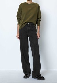 Sudadera verde oliva con mangas raglán, combinada con vaqueros negros de talle alto y corte holgado. Zapatos de plataforma gruesa en negro.