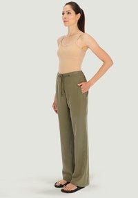 Leichtgewichtige, olivgrüne, weit geschnittene Hosen mit Zugbandsbund, seitlichen Taschen; kombiniert mit einem eng anliegenden, nude-farbenen Tank-Top und schwarzen Sandalen.