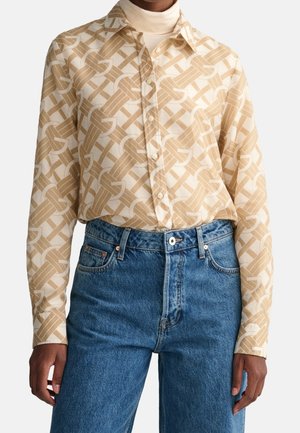 Langærmet beige og hvid mønstret skjorte med knapper, båret over en cremefarvet rullekrave med blå højtaljede jeans.