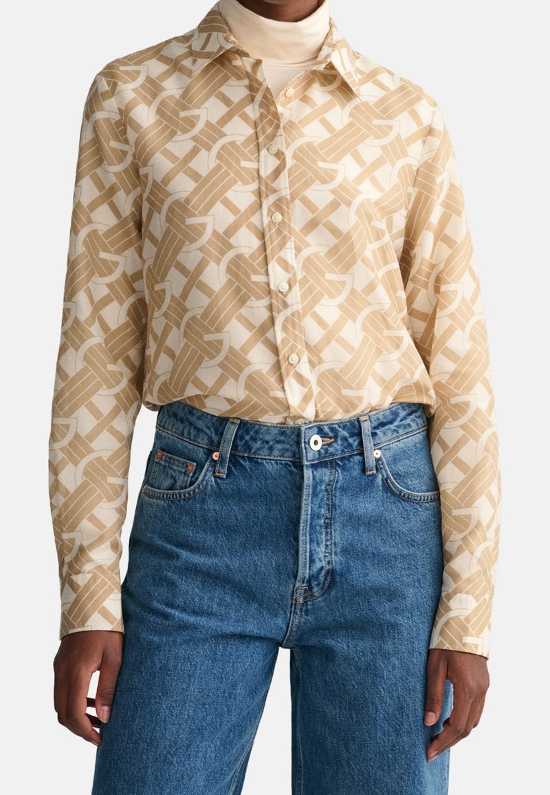 Chemise à manches longues beige et blanche à motifs, boutonnée, portée sur un col roulé crème avec un jean bleu taille haute.