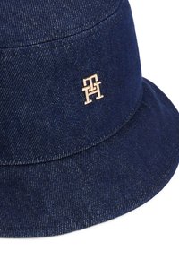 Chapeau seau en denim bleu marine avec un bord légèrement évasé, accentué d'un logo métallique doré. Tissu texturé avec de légères rayures verticales.