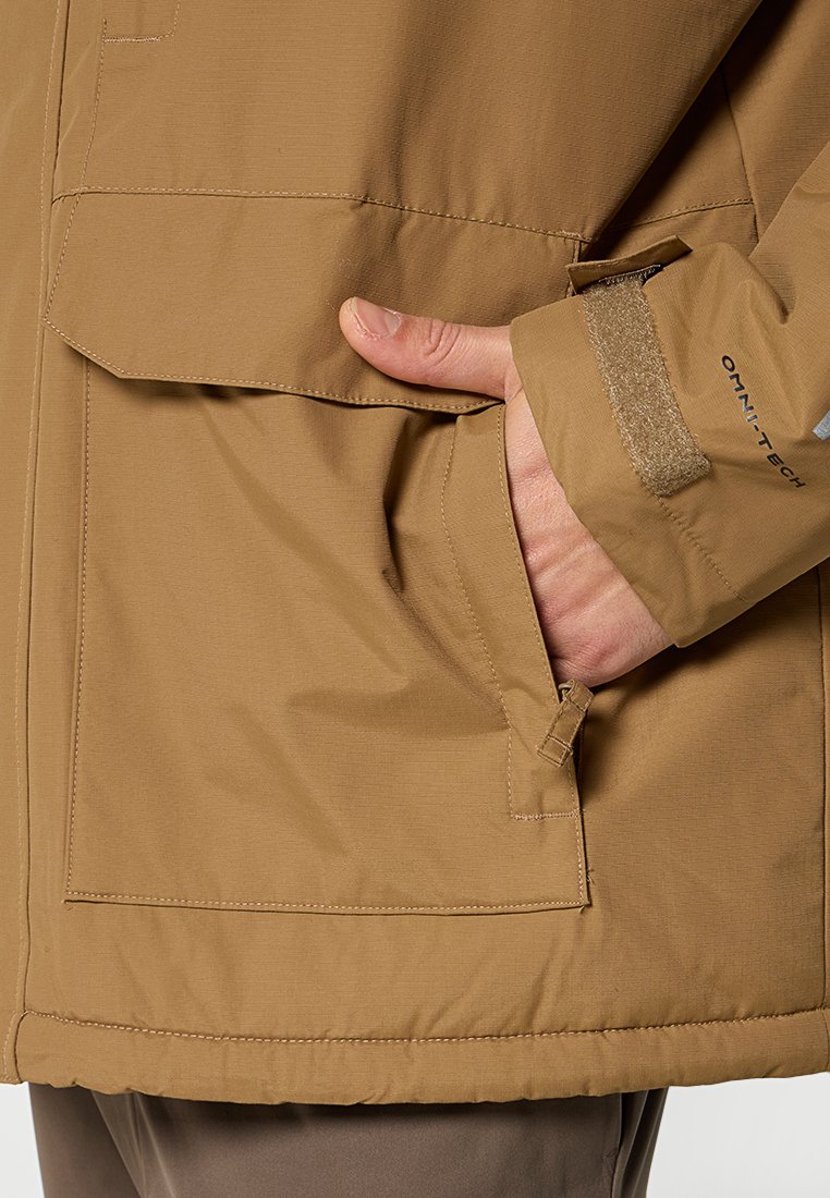 Veste imperméable marron avec une finition texturée, dotée d'une poche latérale, de poignets ajustables et de détails de marque sur la manche.